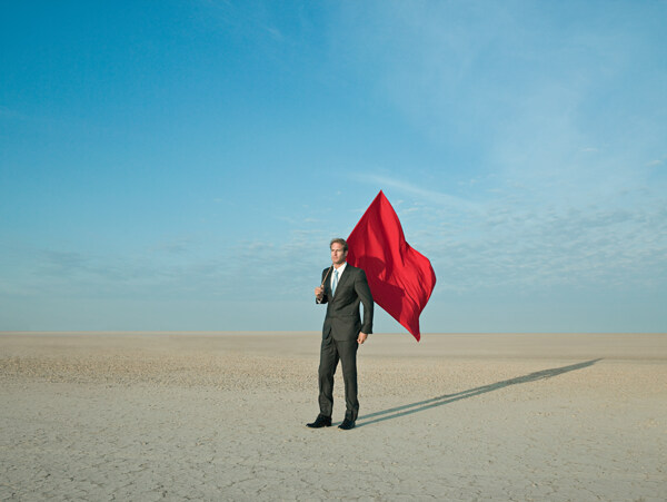 扛着红旗站在沙漠中的商业男人图片