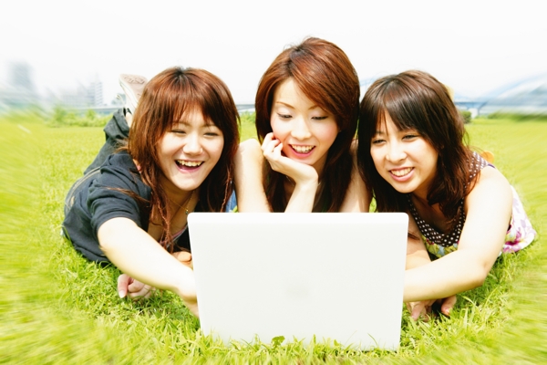 草地上开心玩电脑的三个美女图片