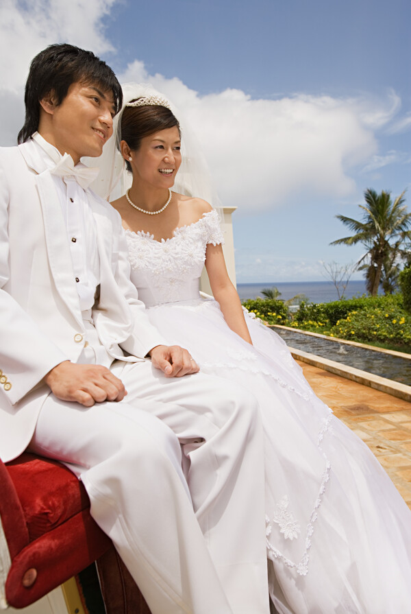穿着洁白婚纱礼服的男女坐在海边远望图片图片