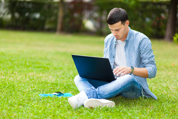坐在草地上的玩电脑男人图片