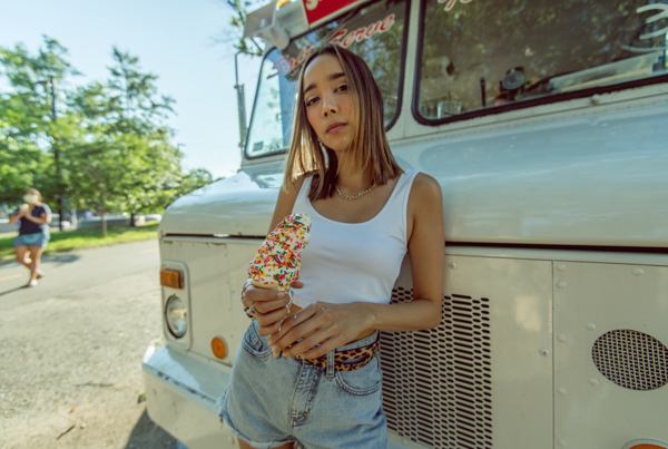 一个穿白T金发美女拿着一个洒满彩针的冰淇淋站在汽车旁